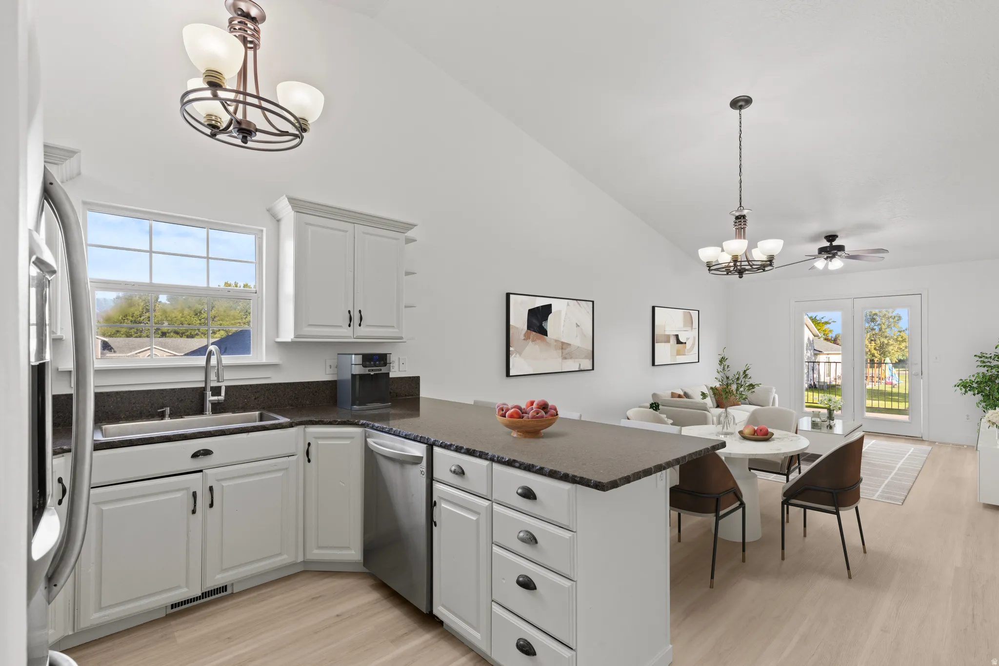 White cabinetry with dark hardware, stainless steel appliances, dark countertops, and wood-finish flooring