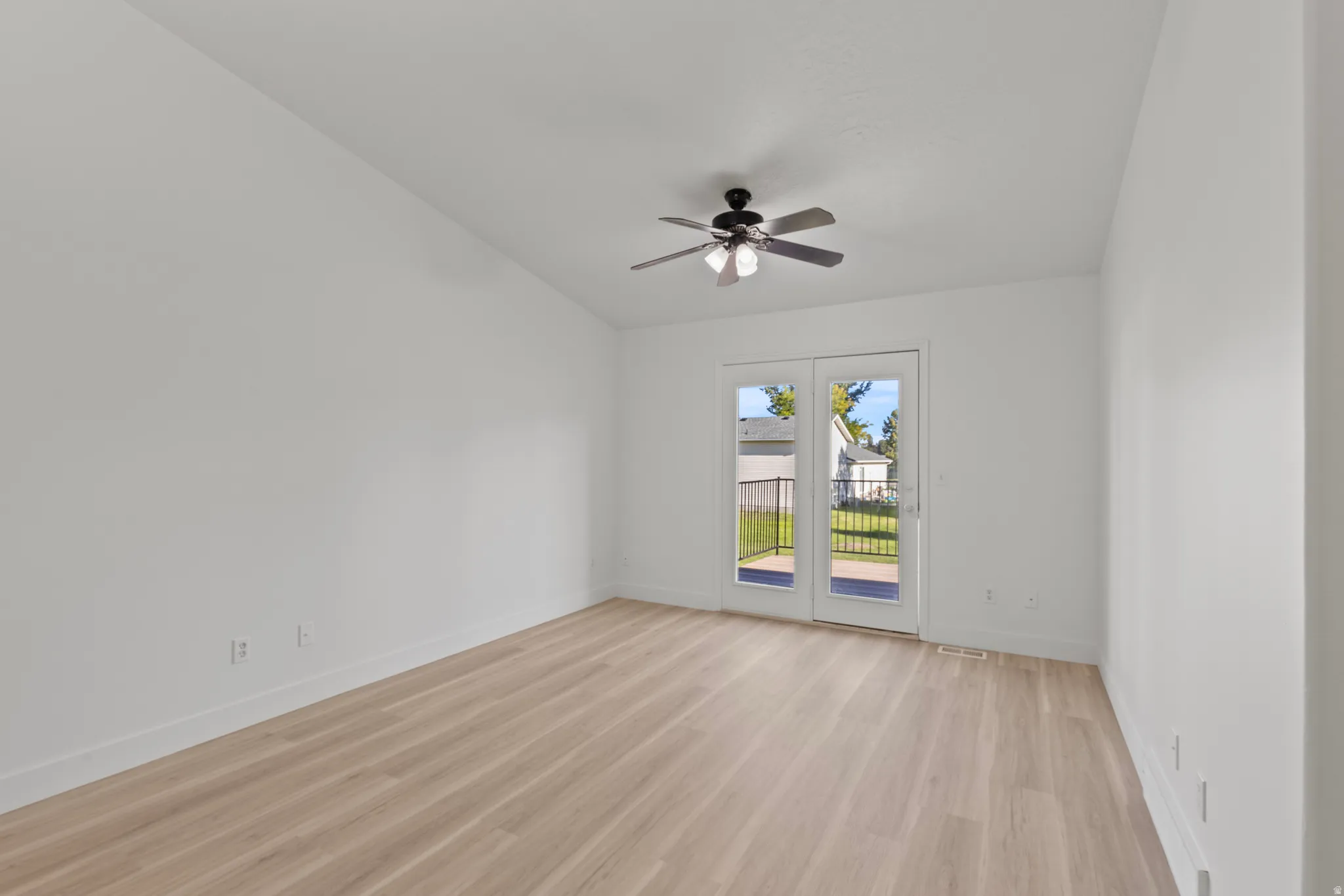 Vaulted ceiling, wood-finish flooring, white walls, ceiling fan, and double glass patio doors
