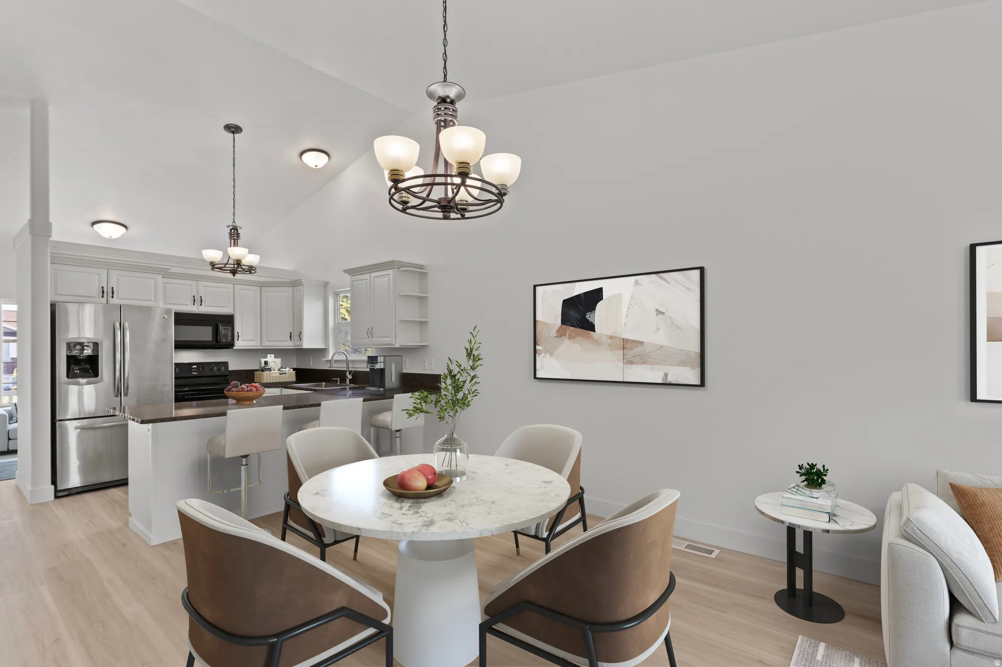 Vaulted ceiling with decorative light fixtures, kitchen featuring stainless steel appliances, light wood-finish flooring, and white cabinetry