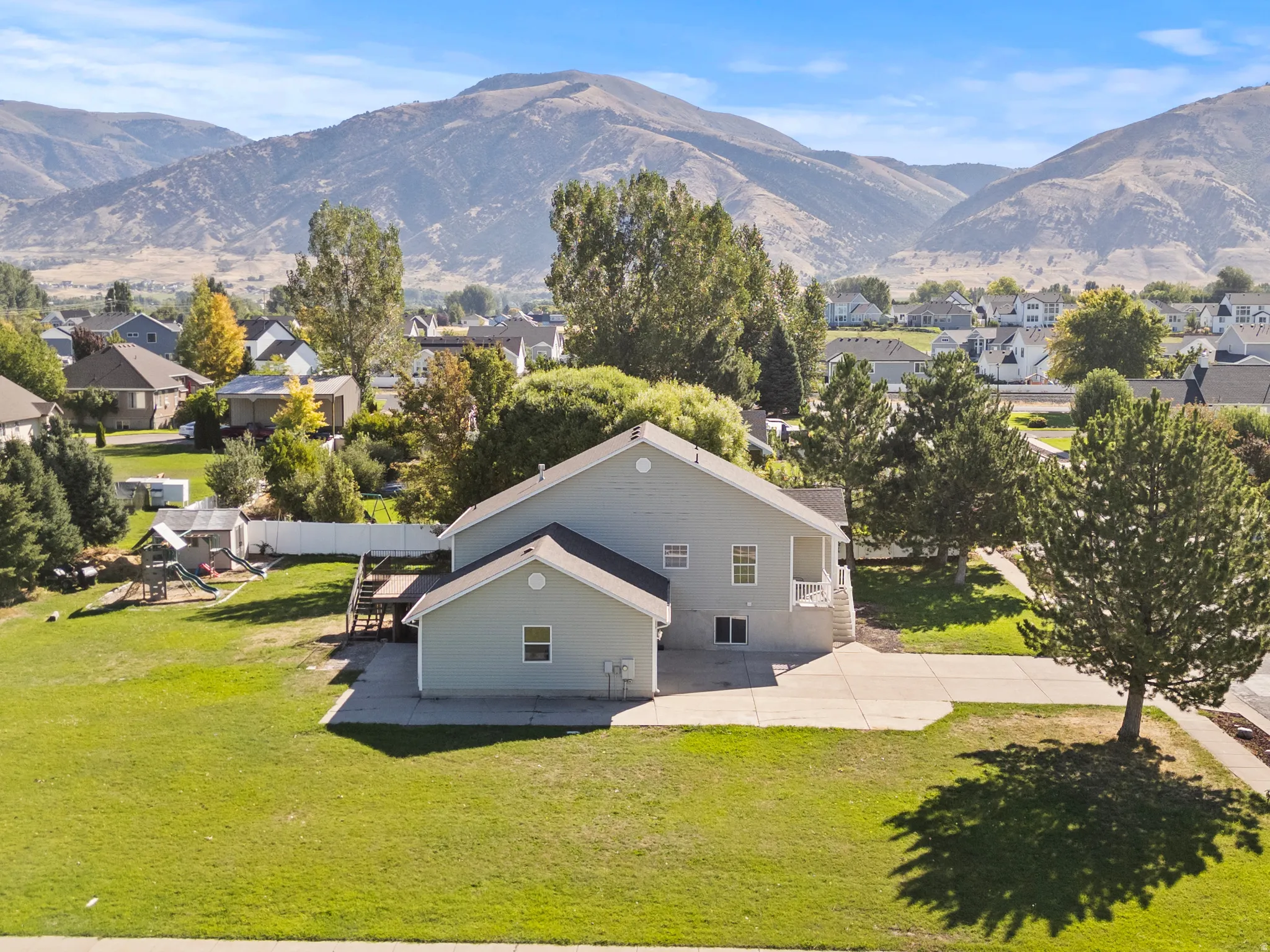 Expansive green lawn, concrete patio, mature trees, and mountain backdrop