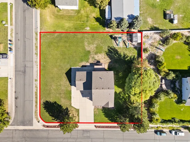 Expansive lot with a spacious grassy area, paved driveway, mature trees, and direct street access