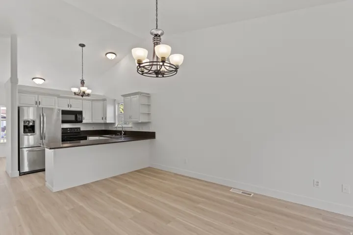 Vaulted ceilings with multiple light fixtures, light wood-finish flooring, white cabinetry, dark countertops, and stainless steel appliances