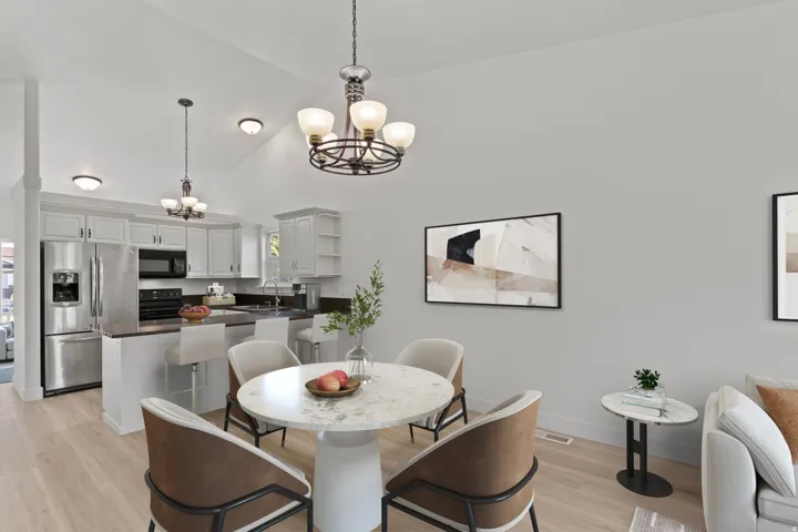 Vaulted ceiling with decorative light fixtures, kitchen featuring stainless steel appliances, light wood-finish flooring, and white cabinetry