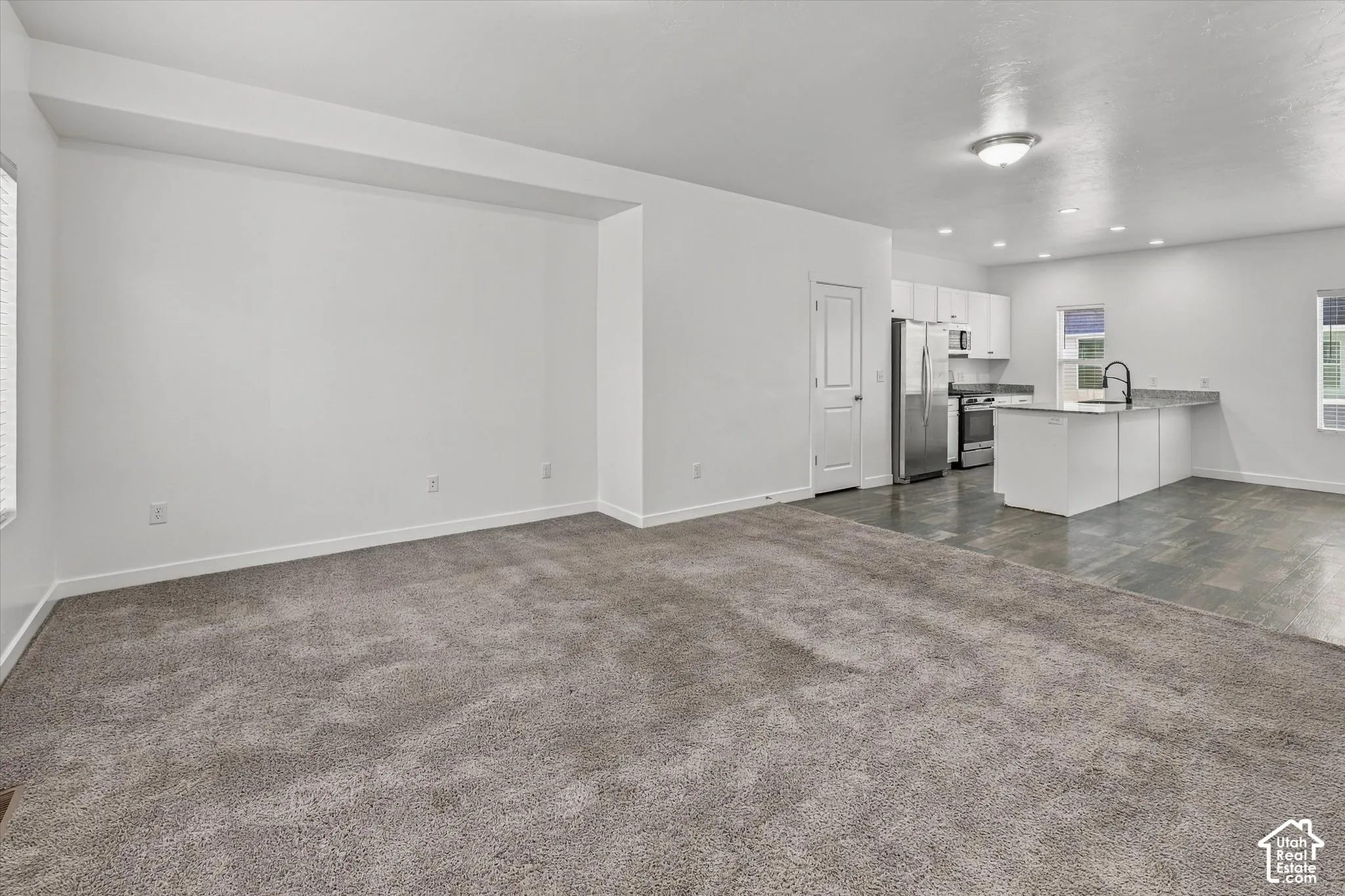 Open-concept floor plan featuring wall-to-wall carpeting, tile flooring in the kitchen area, an island with stone-surface countertop, white cabinetry, and stainless steel appliances