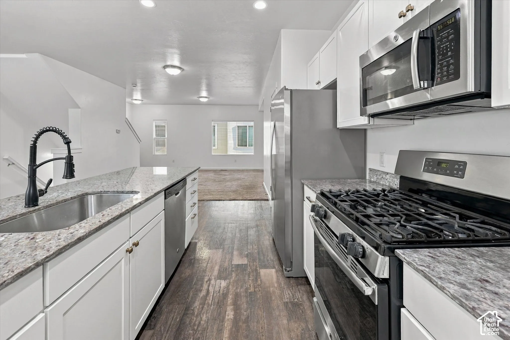 Kitchen featuring white cabinetry, stone-finish countertops, stainless steel appliances, a high-arc faucet, and wood-finish flooring