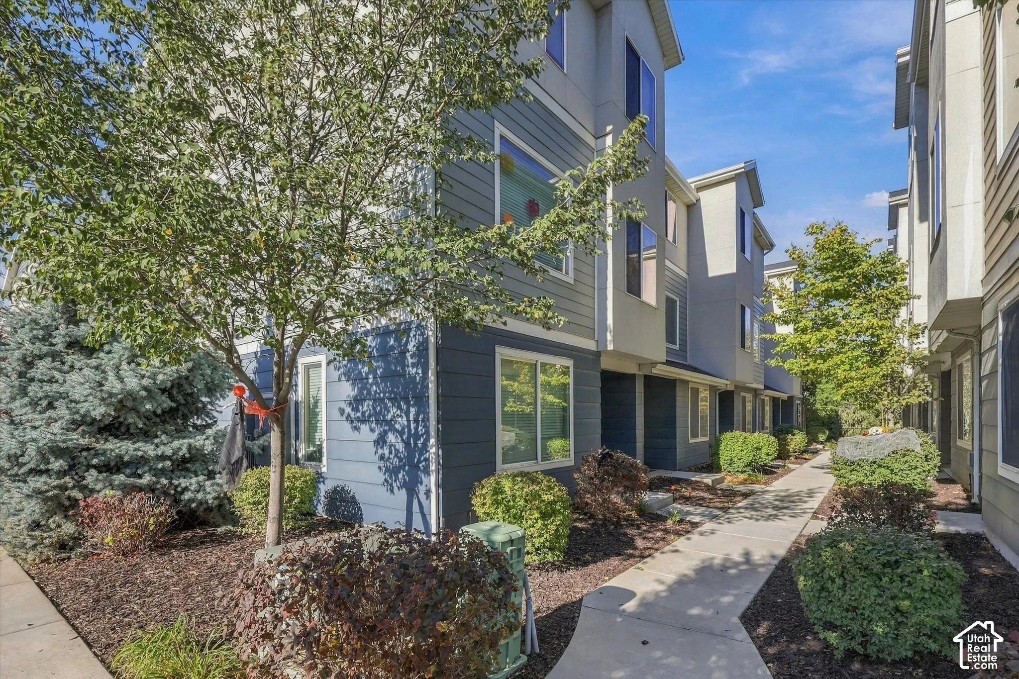 Multi-story exterior featuring fiber-cement siding, composite shingles, and a paved walkway bordered by mature landscaping