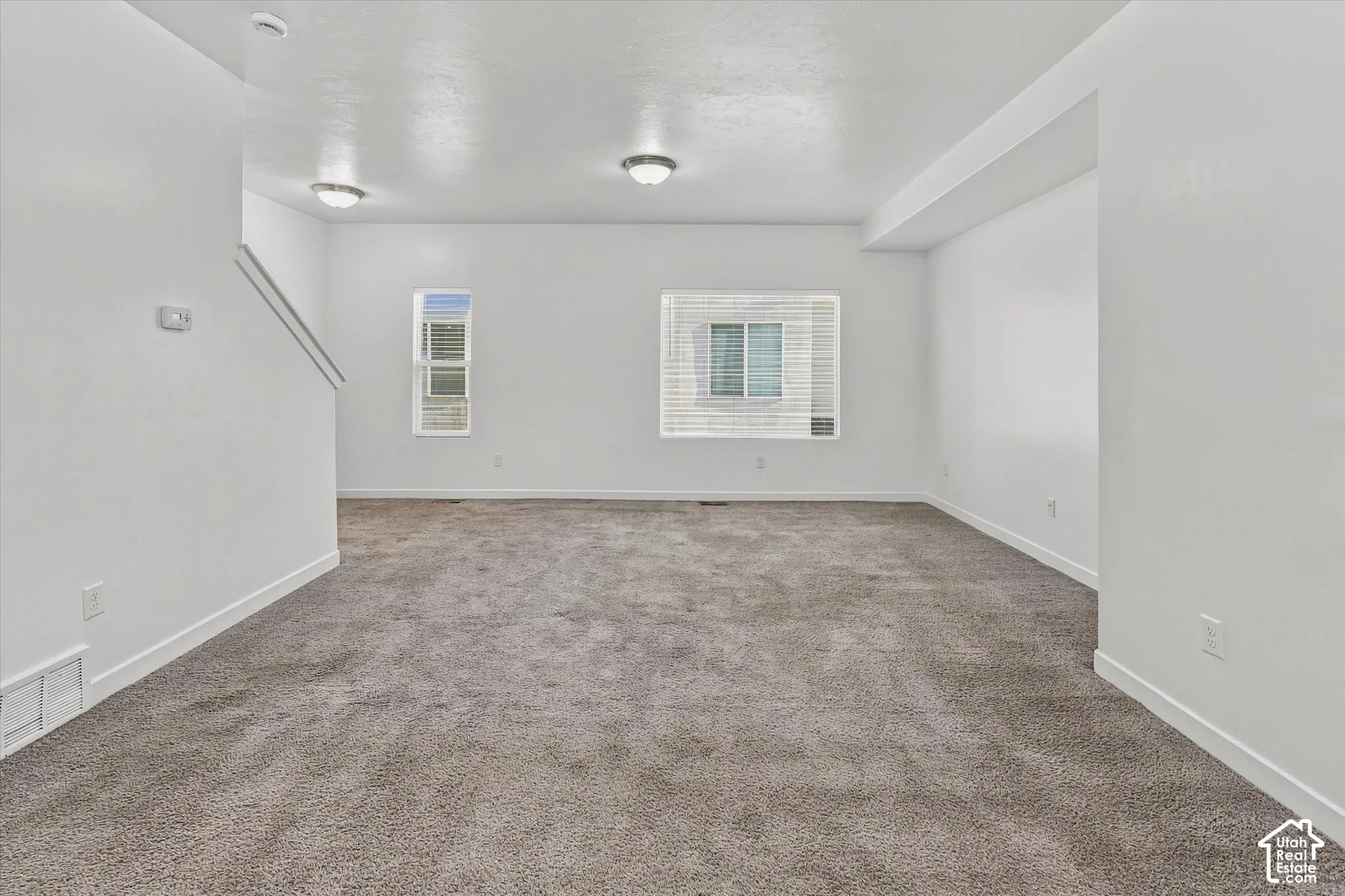 Open interior space featuring neutral wall-to-wall carpeting, crisp white walls, dual flush-mount ceiling light fixtures, and multi-pane windows