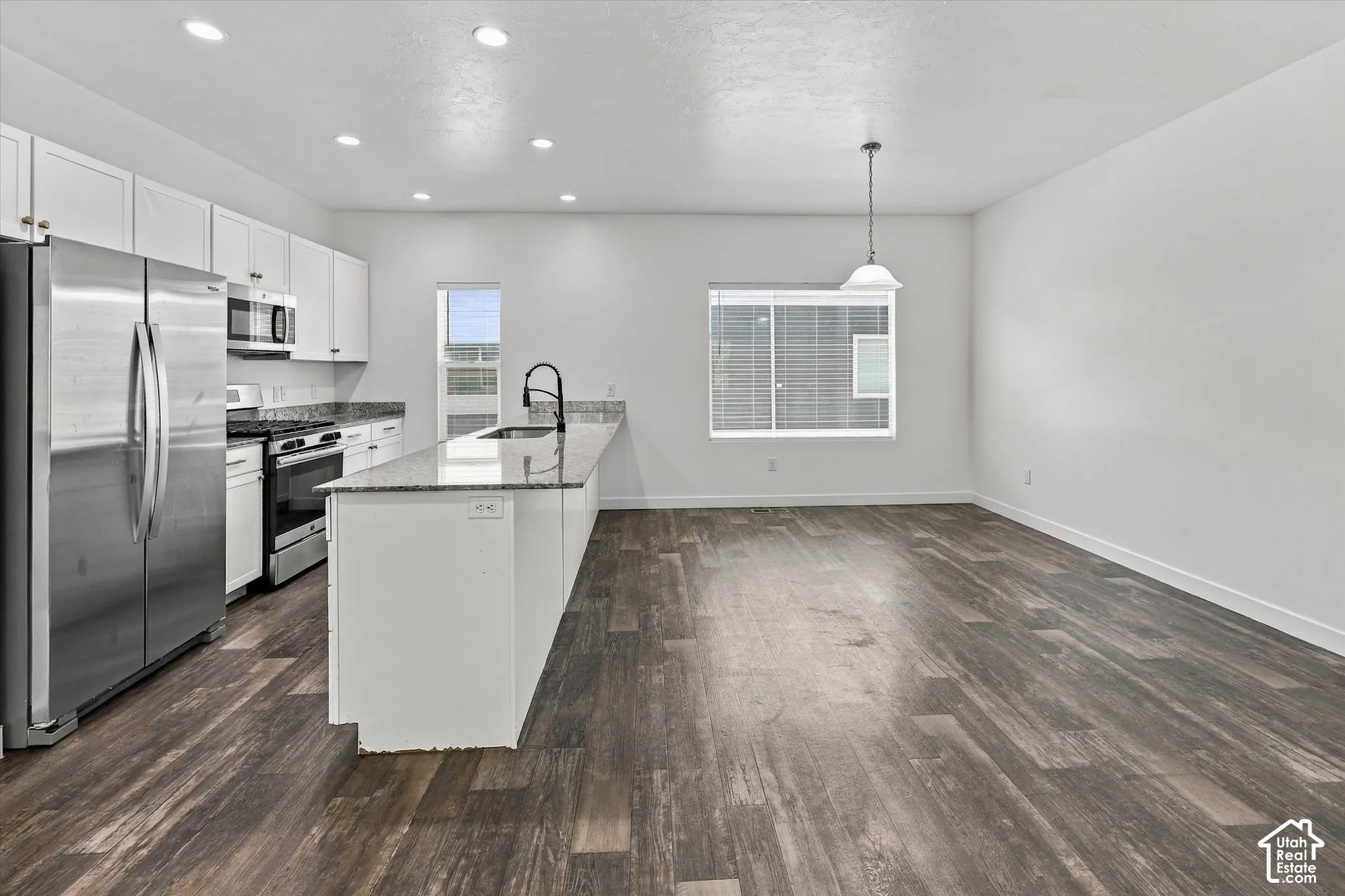 Kitchen featuring white cabinetry, stone-finish countertops, stainless steel appliances, a kitchen island with an integrated sink, and wood-finish flooring