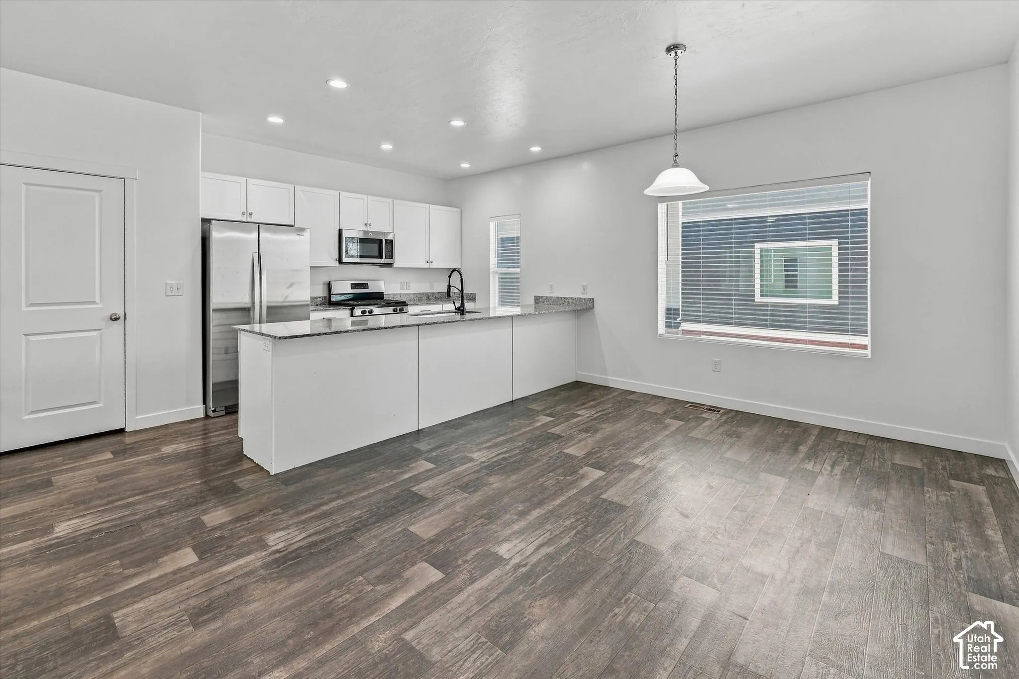 Kitchen featuring white cabinetry, stone-finish countertops, stainless steel appliances, a peninsula island, and wood-finish flooring