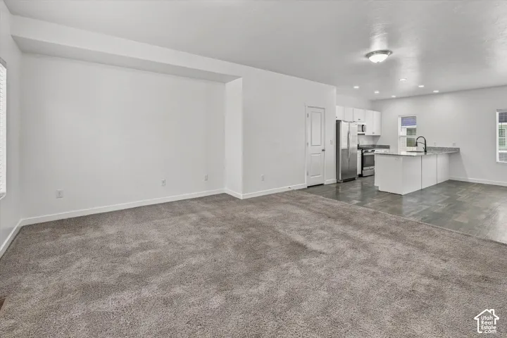 Open-concept floor plan featuring wall-to-wall carpeting, tile flooring in the kitchen area, an island with stone-surface countertop, white cabinetry, and stainless steel appliances