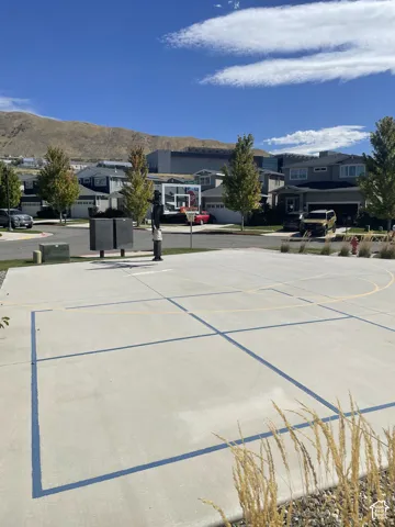 Paved recreational court with basketball hoop, surrounded by residential street, landscaping, and distant mountains