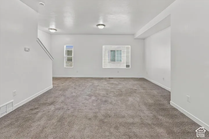 Open interior space featuring neutral wall-to-wall carpeting, crisp white walls, dual flush-mount ceiling light fixtures, and multi-pane windows