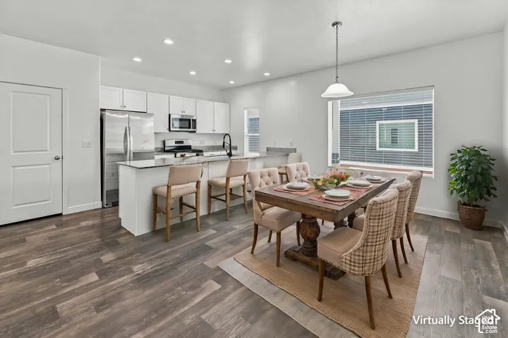 Kitchen featuring white shaker cabinetry, stone-finish countertops, stainless steel appliances, a peninsula with bar seating, and wood-finish flooring