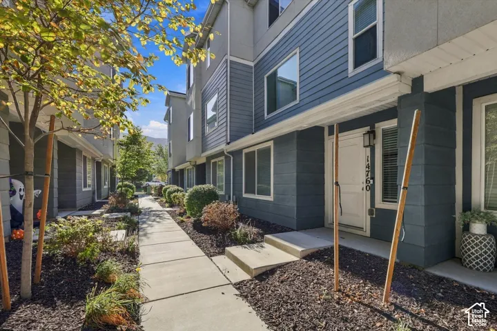 Multi-story exterior featuring blue horizontal and vertical siding, concrete walkway, and landscaped garden beds with dark mulch