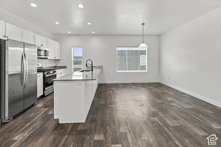 Kitchen featuring white cabinetry, stone-finish countertops, stainless steel appliances, a kitchen island with an integrated sink, and wood-finish flooring