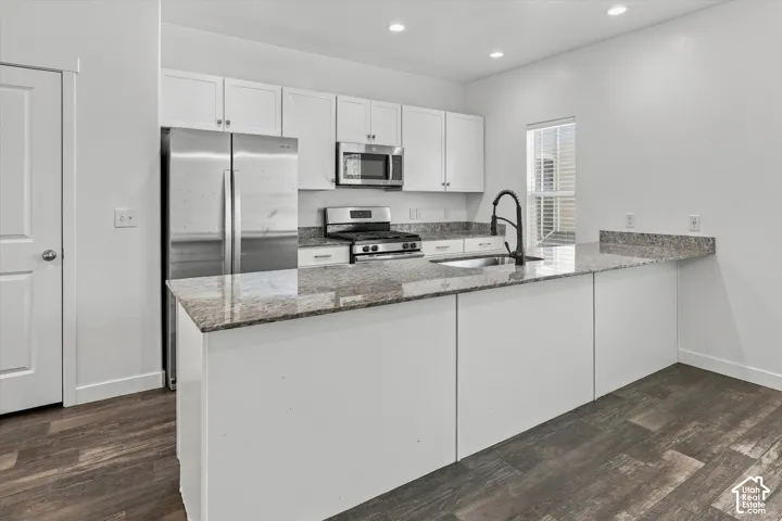 Kitchen featuring white cabinetry, stone-surface countertops, stainless steel appliances, a high-arc matte black faucet, and wood-finish flooring