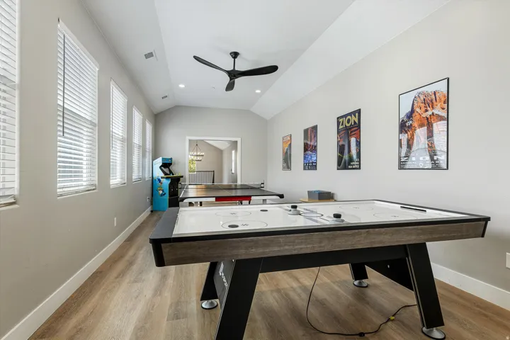 Vaulted ceiling with a ceiling fan, multiple windows with blinds, wood-finish flooring, and recessed lighting