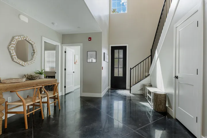 Vaulted entry with black-framed door, black metal stair railing, and dark polished concrete flooring