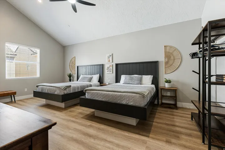 Vaulted ceiling with a ceiling fan, wood-finish flooring, and a large window with blinds