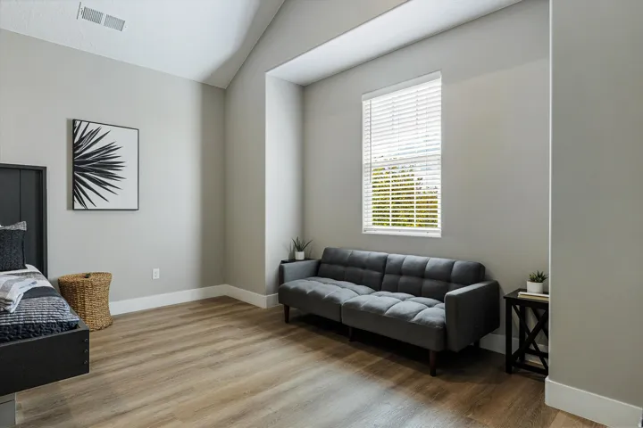 Vaulted ceiling with sloped design, light wood-finish flooring, single window with blinds, neutral wall paint, and white trim