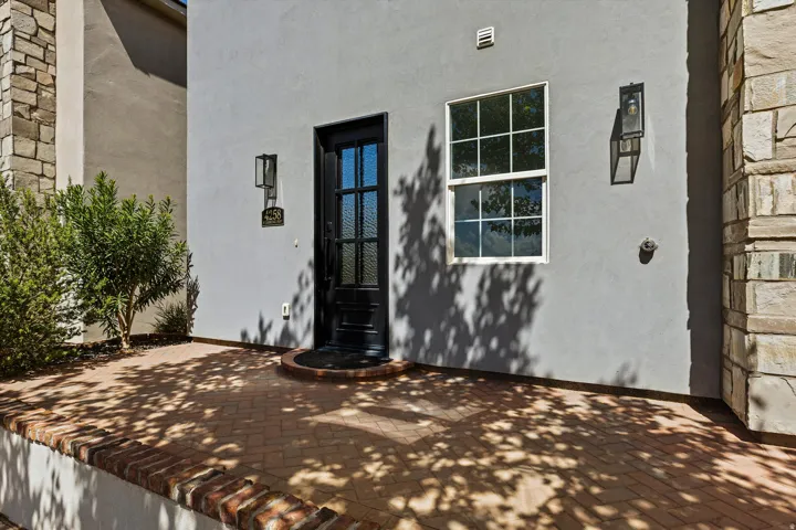 Stucco exterior with stone accents, brick paver patio, dark paneled entry door, and exterior wall lanterns