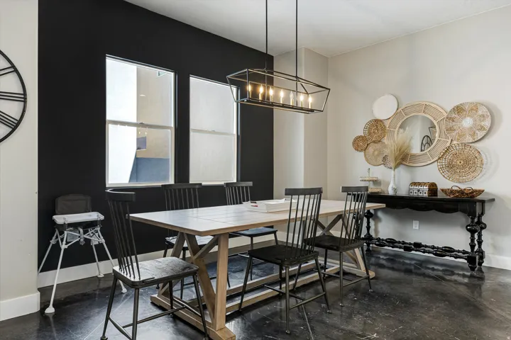 Distinguished dining area featuring dark accent wall, two large windows, a geometric linear chandelier, and dark-toned flooring