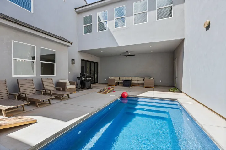 Private courtyard featuring a rectangular pool with integrated steps, a covered patio area with an attached ceiling fan, and concrete hardscaping
