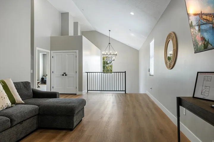 Vaulted ceilings with recessed lighting, wood-finish flooring, white double doors with black hardware, black metal railing, and a window with blinds