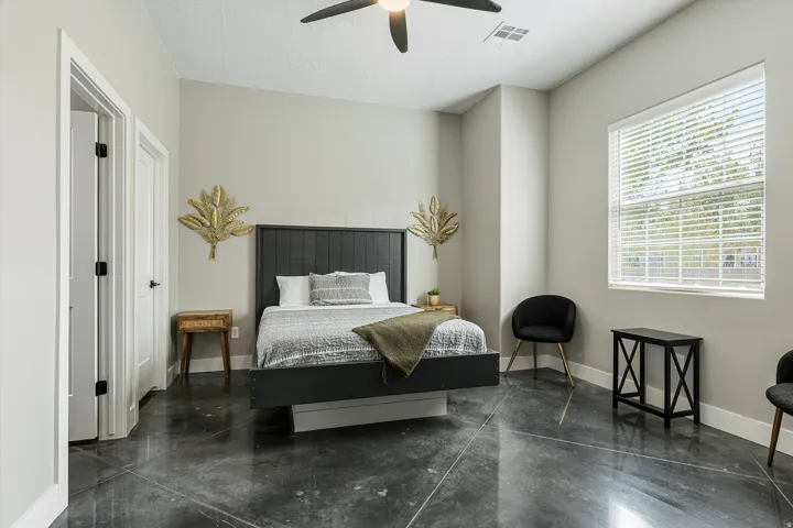 Polished concrete flooring, high ceilings with ceiling fan, ample natural light from large window, white trim, and white doors with black hardware