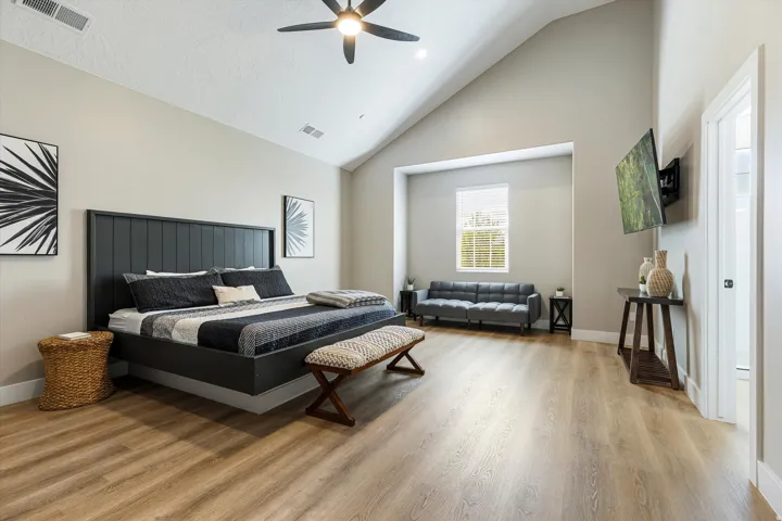 Vaulted ceiling with a ceiling fan, wood-finish flooring, and a large window with blinds