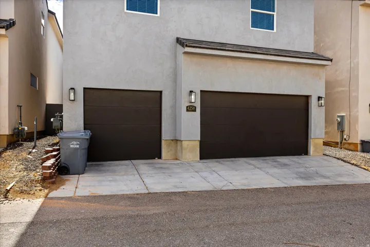 Stucco exterior with two dark-toned garage doors, concrete driveway, and exterior wall sconces