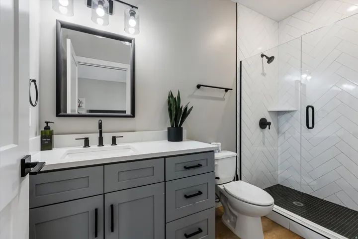 Vanity with a white countertop and matte black fixtures, framed mirror, and a walk-in shower with white herringbone tile and dark flooring