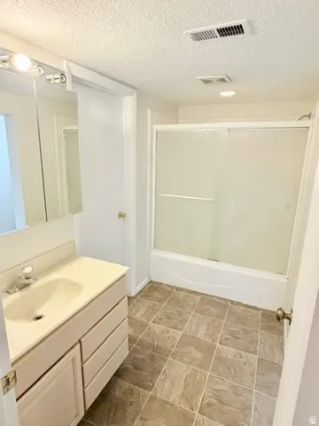 Bathroom featuring a single vanity with integrated sink, a built-in bathtub with sliding glass doors, and tile flooring