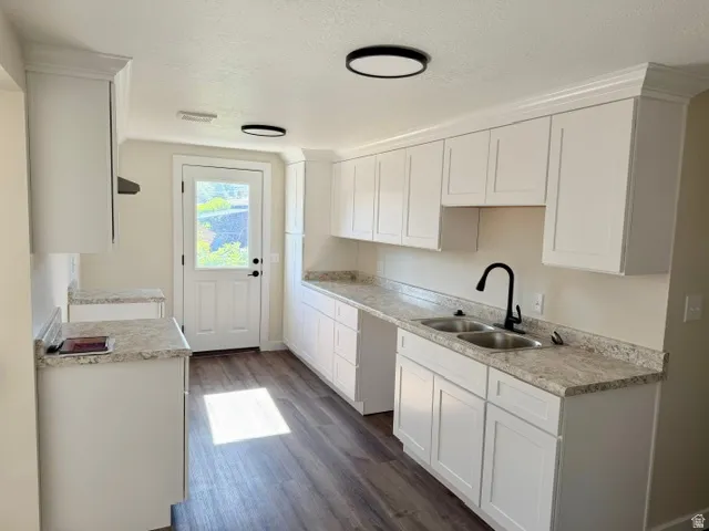 White shaker cabinetry with crown molding, dual basin stainless steel sink, matte black gooseneck faucet, and wood-finish flooring