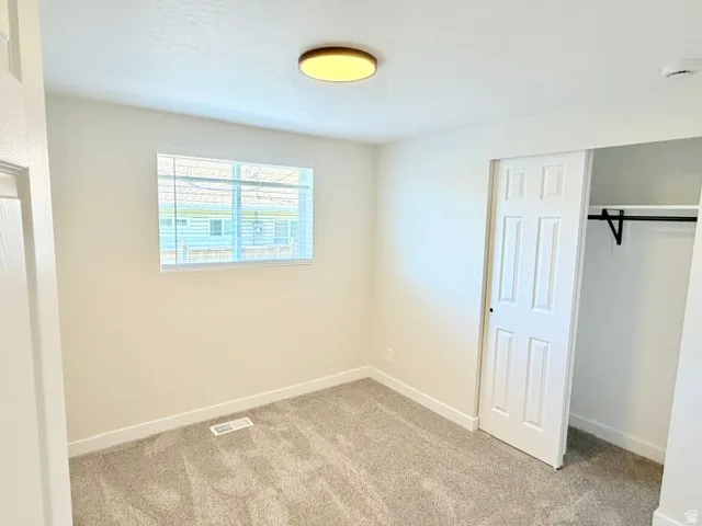 Carpeted room featuring a window with blinds, ceiling-mounted light fixture, and a bi-fold closet with an interior rod