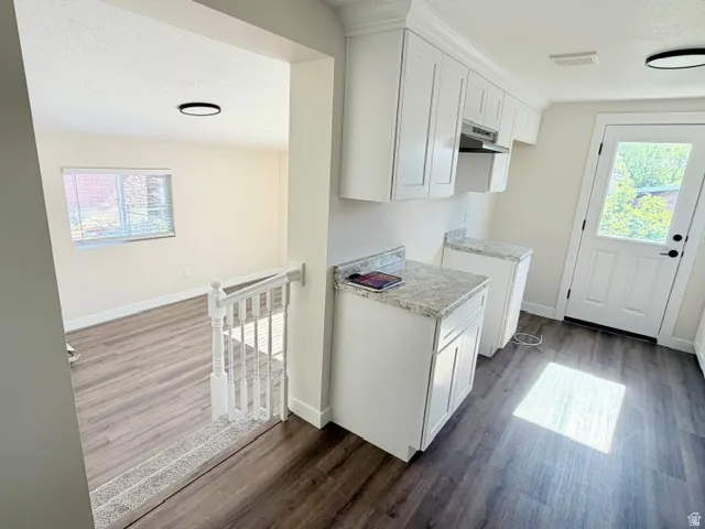 White shaker cabinetry with stone-finish countertops, wood-finish flooring, and a white paneled door with a glass insert
