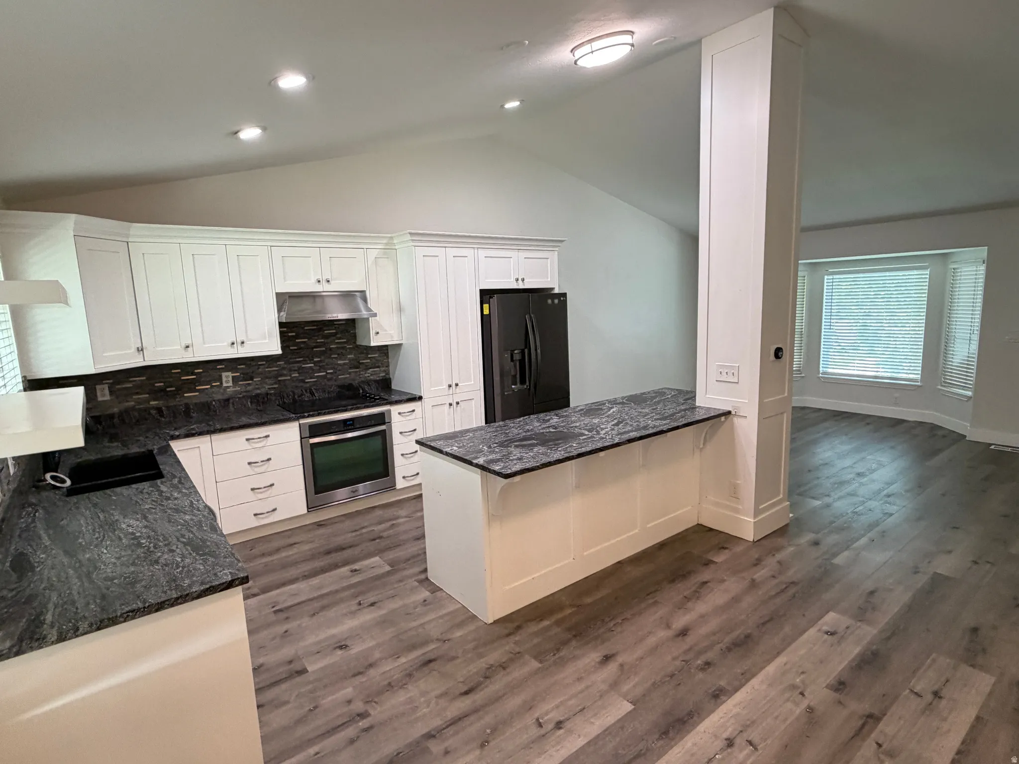 White cabinetry with dark contrasting countertops, stainless steel appliances, wood-finish flooring, recessed lighting, and a bay window