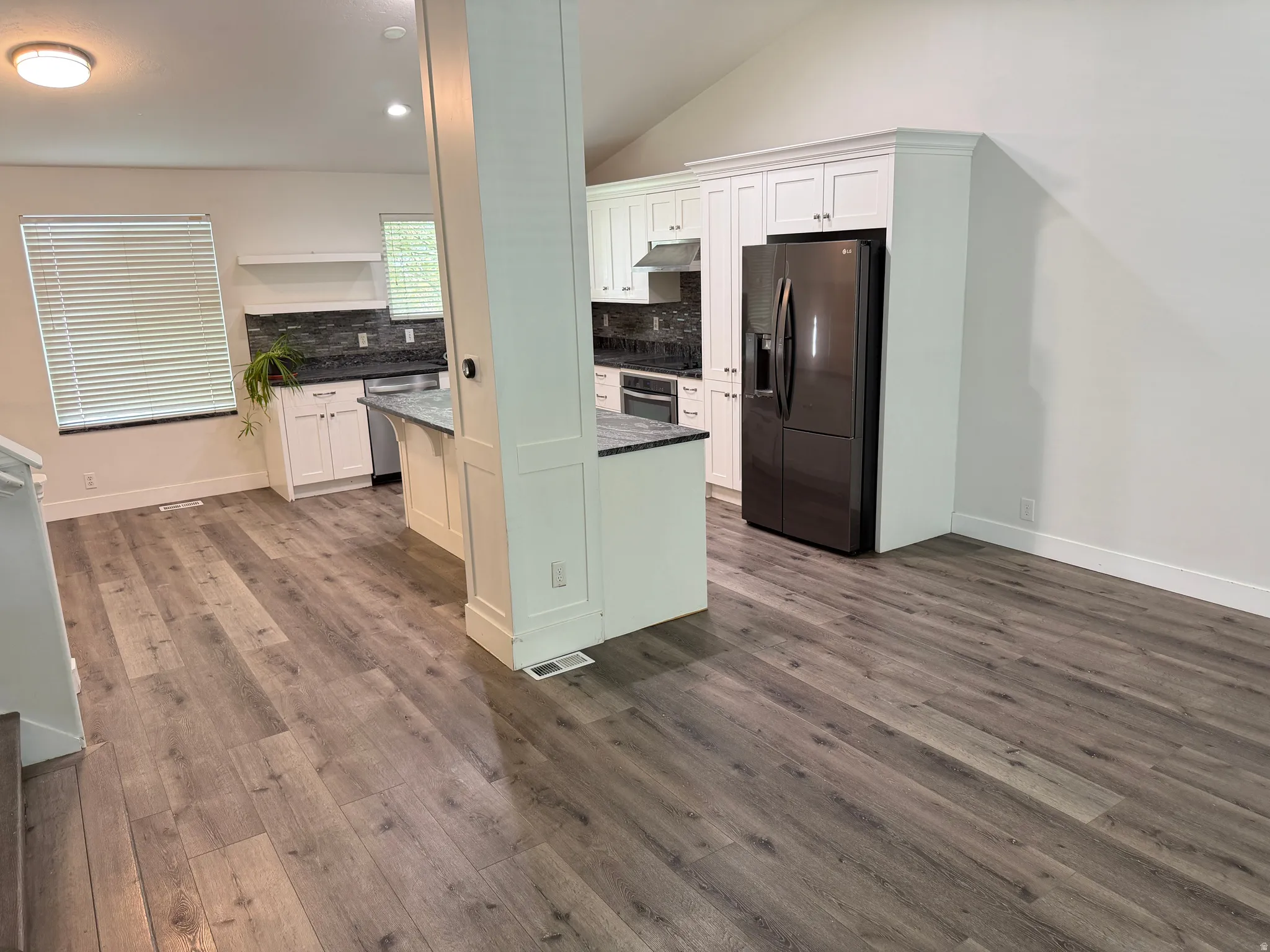 Wood-finish flooring throughout, vaulted ceiling, white cabinetry, dark stone countertops, and a dark tile backsplash