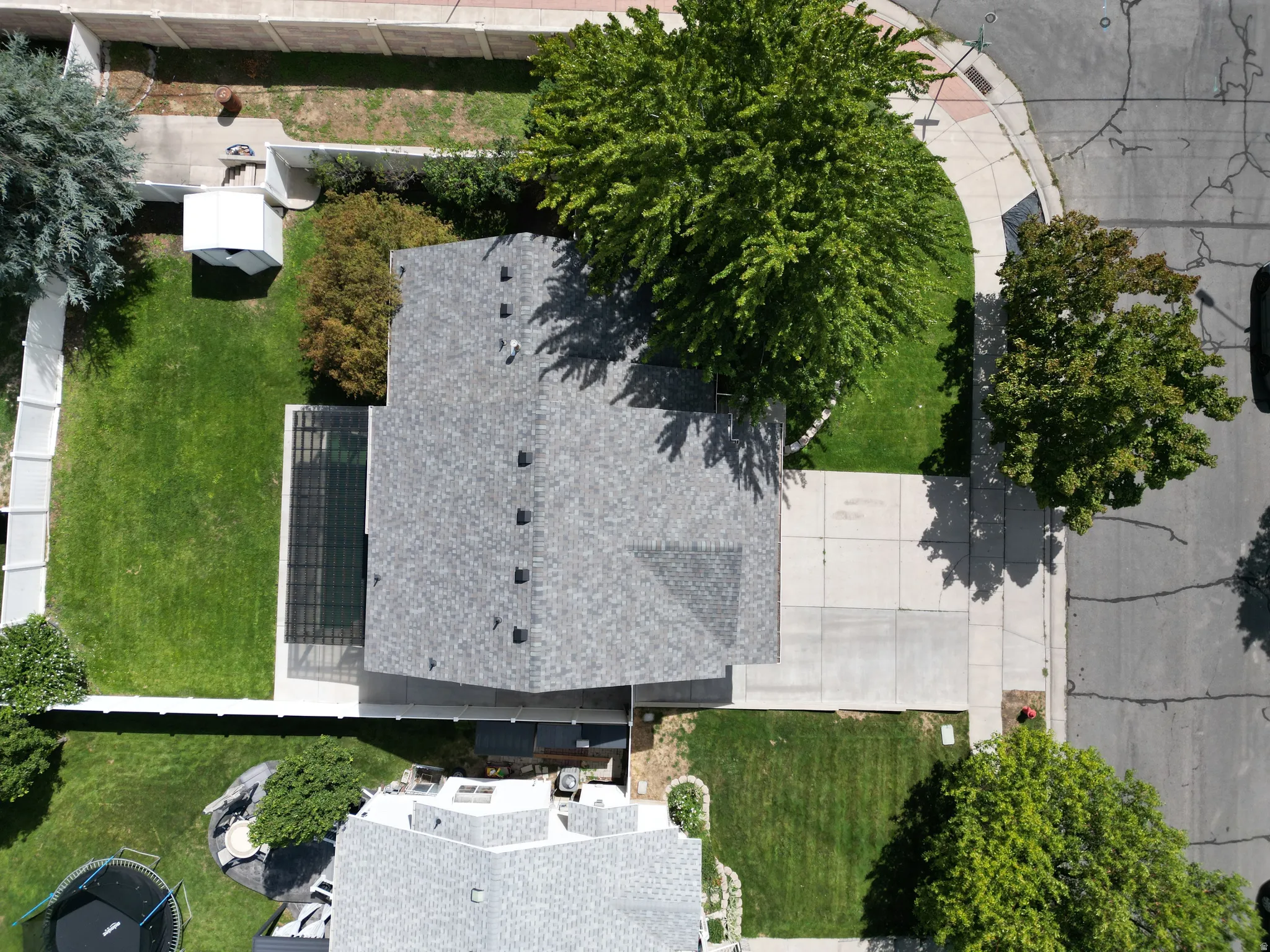 Asphalt shingle roof, paved driveway, concrete sidewalks, established trees, and grassy lawn areas