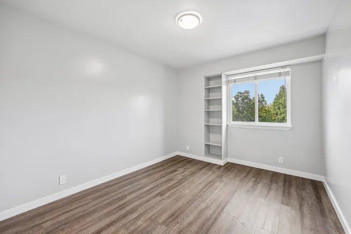 Wood-finish flooring, built-in shelving, white trim, and a flush-mount ceiling light