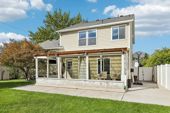 Rear exterior with light-toned siding, a covered patio structure, multiple windows, and a concrete pad
