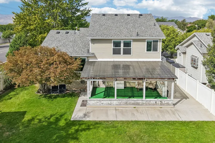 Two-story residence with a gray shingle roof, neutral-toned siding, a covered patio with a translucent roof, and a fenced backyard with mature trees and a concrete patio