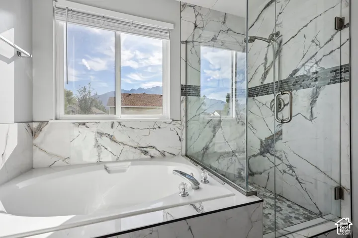 Soaking tub with deck-mounted fixtures, glass-enclosed shower with mosaic tile accents, and large window with mountain scenery
