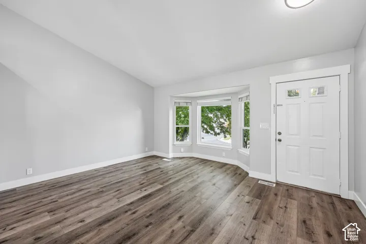 Wood-finish flooring, bay window, vaulted ceiling, recessed lighting, and a paneled entry door