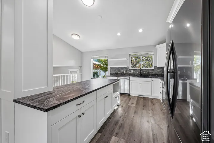 Kitchen featuring white shaker cabinetry, dark patterned countertops, stainless steel appliances, and wood-finish flooring