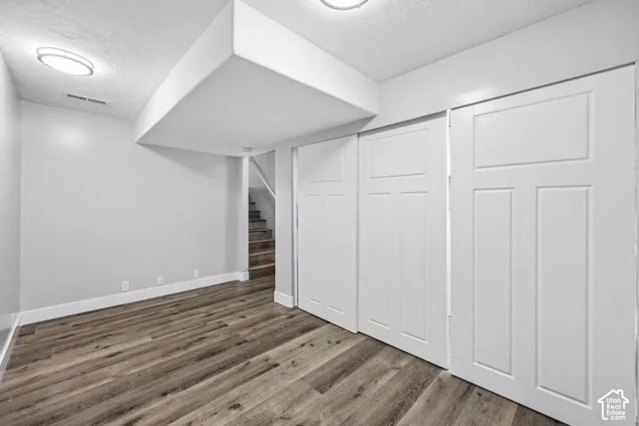 Wood-finish flooring with white trim, white walls, and built-in closet doors