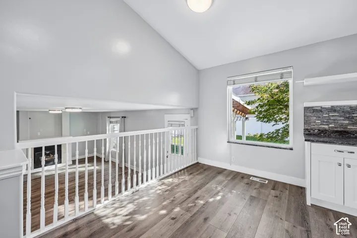 Vaulted ceiling with a flush-mount light fixture, wood-finish flooring, white railing, and a window with blinds