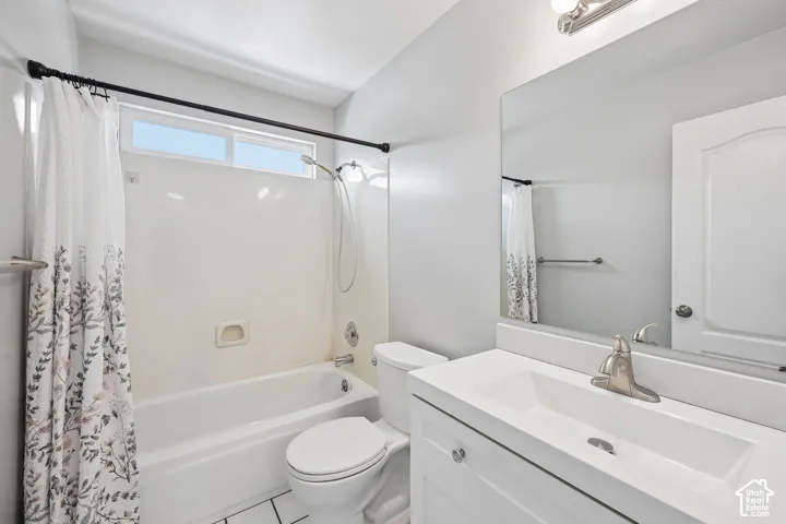 Bathroom featuring a white vanity with integrated sink, brushed nickel faucet, full-width mirror, and a shower-tub combination with an overhead window