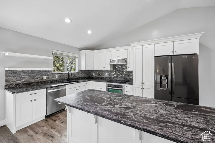 Kitchen featuring white cabinetry, dark patterned countertops, a stone tile backsplash, stainless steel appliances, and a central island