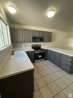 U-shaped kitchen featuring grey cabinetry, light-toned countertops, a stainless steel range, a built-in microwave, and tile flooring